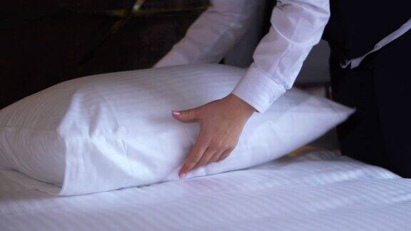 在一个小而舒适的旅馆房间里一位旅馆清洁女工正在整理枕头