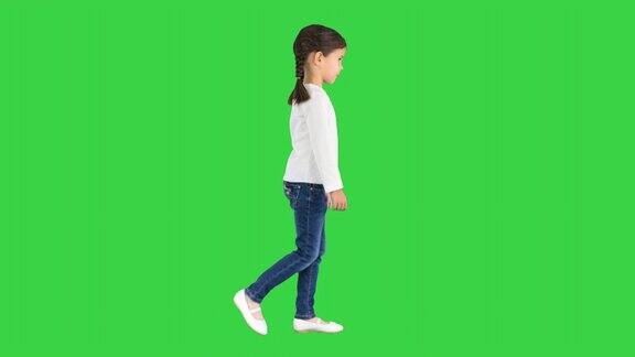 小女孩梳着猪尾巴穿着白色长袖上衣和牛仔裤走在绿屏上