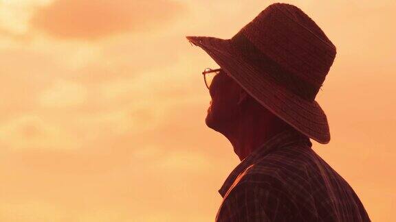 夕阳下老农民站在稻田里的剪影一位戴着帽子的老人在金色的天空背景上望着远方