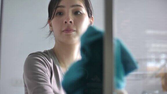 戴手套的亚洲女人用抹布擦窗户