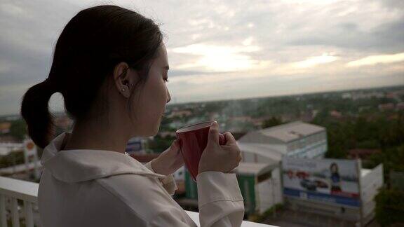 一个亚洲女人在阳台上喝着咖啡欣赏风景的场景