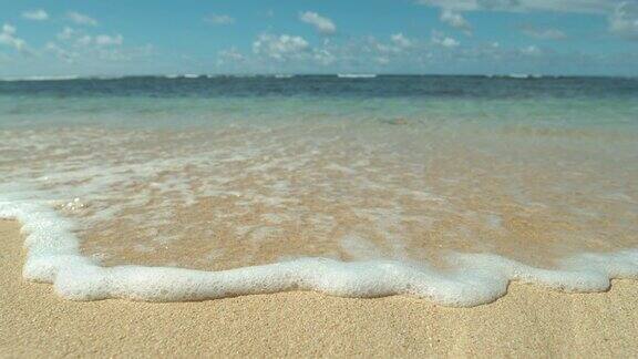 慢镜头特写:阳光明媚的日子里充满异国情调的海滩正被泡沫的海浪冲刷着