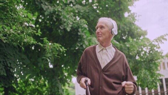 开朗的男老人戴着耳机拄着拐杖在公园跳舞心情好