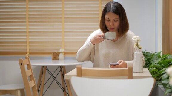 咖啡馆里一位女士在喝咖啡时在木桌上触摸智能手机