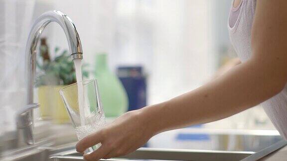 年轻女子在厨房里用水龙头往杯子里注水