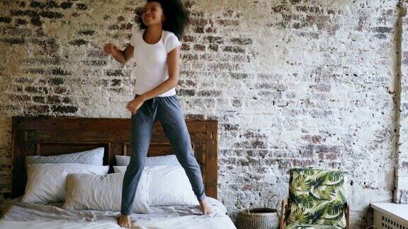 卷毛混血年轻快乐的女孩有乐趣跳舞在床上在家