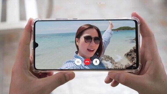 手握智能手机而快乐的亚洲女人自拍视频在海滩上