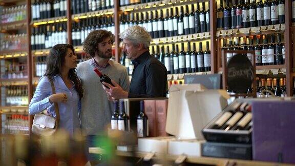 一对情侣在一家葡萄酒商店微笑着向酒庄老板询问葡萄酒的属性