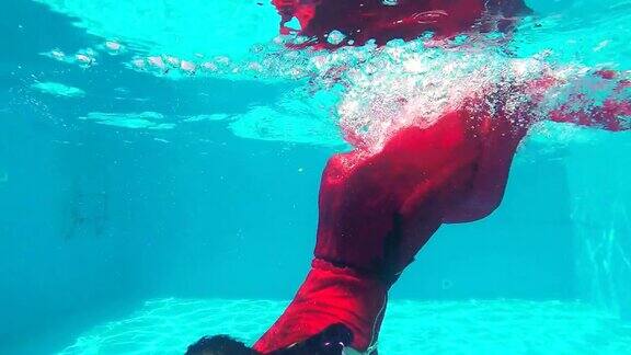 一个扎着辫子穿着红色长裙的年轻女孩在游泳池的水下游泳