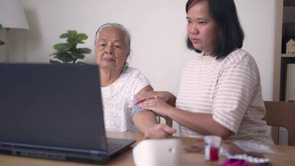 一名妇女帮助祖母测量血压并使用笔记本电脑与医生进行视频通话