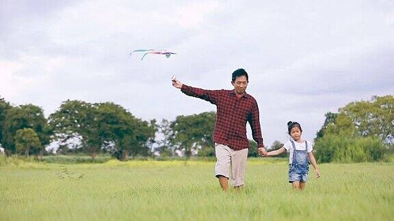亚洲的孩子女孩和父亲与风筝跑和快乐的草地在夏季的自然