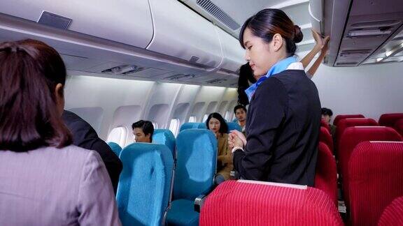 在登机过程中穿着制服的美丽的亚洲空姐欢迎乘客帮助他们找到座位并把行李放在头顶的行李柜里