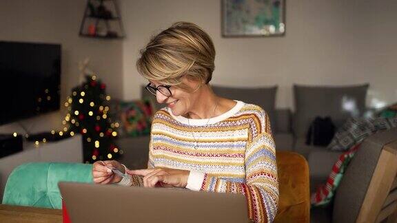一个成熟的女人一边在网上圣诞购物一边输入信用卡信息