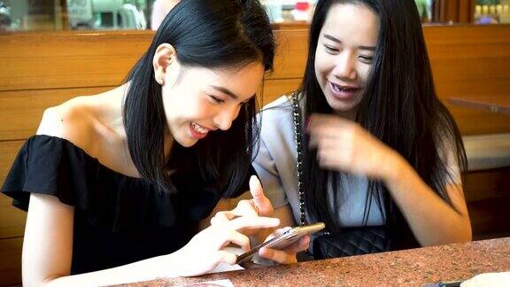 两个亚洲女性朋友用手机一起笑在日本餐厅享受美好时光的女人