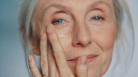 美丽资深女性肖像轻轻涂抹下眼霜使用天然抗老化化妆品使老妇人的皮肤柔软光滑无皱纹产品为美容护肤化妆