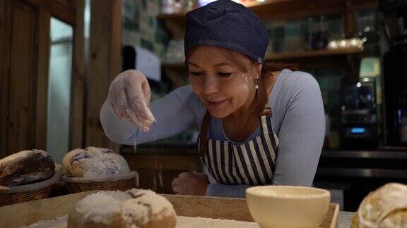 快乐的女面包师在面包店往面包上洒面粉