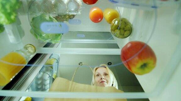 一个年轻女子把食物装进冰箱打开冰箱的门放上刚买的蔬菜内视图