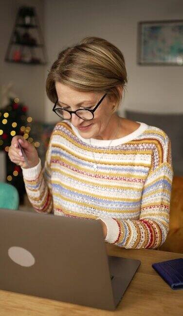 一个成熟的女人一边在网上圣诞购物一边输入信用卡信息