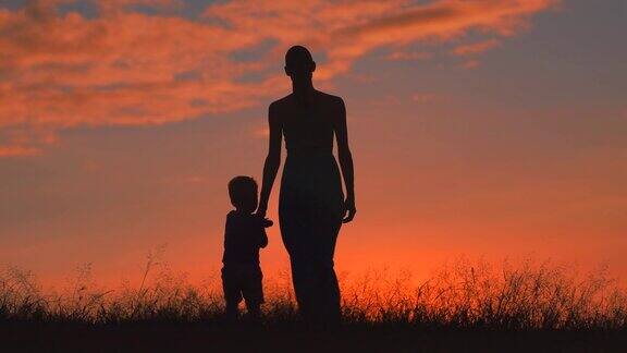 日落时分母亲和孩子在田野里散步手牵着手交谈着