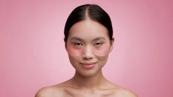 亚洲女性与应用眼袋保湿脸粉红色背景