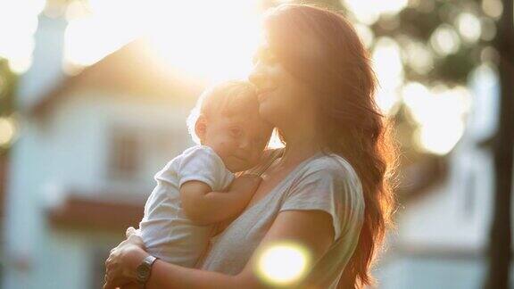 母亲照顾和爱婴儿在日落时间妈妈拥抱和抱着蹒跚学步的儿子在美丽的黄金时间