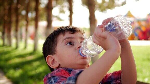 小男孩在公园里喝塑料瓶里的水