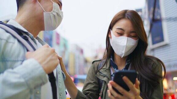 亚洲浪漫情侣戴口罩在城市旅行蜜月旅行新婚男女背包客看手机寻找目的地在疫情期间一起享受假期