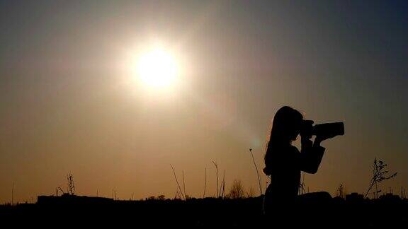 一个夕阳下年轻的女孩摄影师的剪影