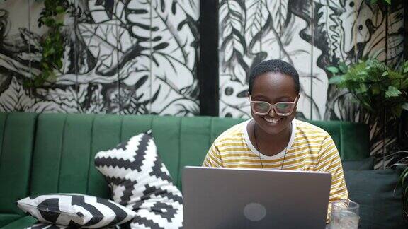 年轻女子一边在咖啡馆用笔记本电脑工作一边用智能手机