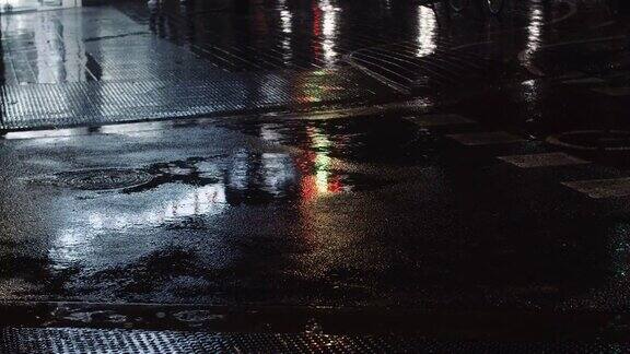 细雨、水坑和夜晚的城市灯光反射在道路上