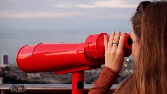 旅游:年轻的女游客在日落时用投币望远镜看城市特写手持慢动作60帧秒