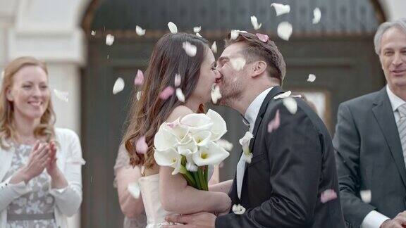 婚礼宾客向亲吻的新婚夫妇投掷花瓣