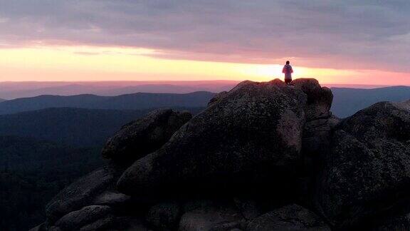 一名孤独男子站在山顶欣赏日落的无人机拍摄