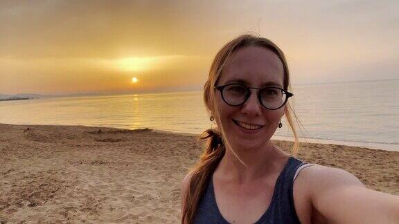 一名女子在海滩度假时拍摄美丽的日落视频自拍