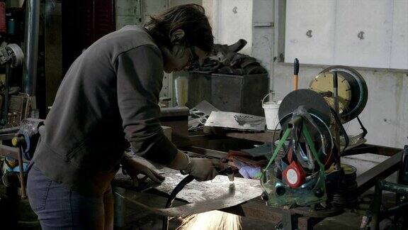 年轻女子铁匠穿着休闲衣服切割铝形状与等离子切割机在她凌乱的车间