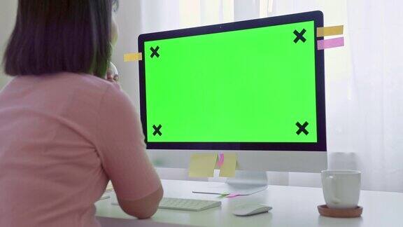 年轻的成年人在她的办公桌前工作在一台模拟绿色屏幕的电脑上过肩镜头她坐在家里的书桌前