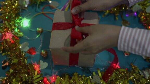 女性双手定型圣诞礼物纸包在桌上女人正在包装礼物盒并把红丝带系在蝴蝶结上