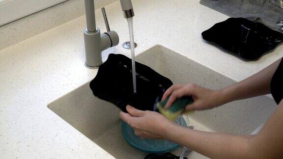 一个女人在厨房水槽的水流下洗盘子有蓝的有黑的特写镜头不知名的概念4k