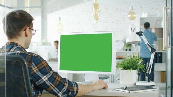 一个人坐在他的桌子上的绿色屏幕电脑的特写背景模糊和明亮的办公室人们通过办公室例行公事