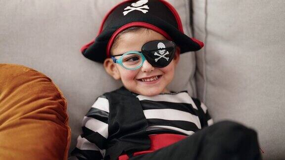 可爱的西班牙男孩穿着海盗服装坐在家里的沙发上