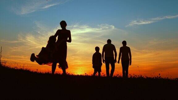 黄昏时分母亲抱着女儿转父亲带着两个儿子在草地上散步