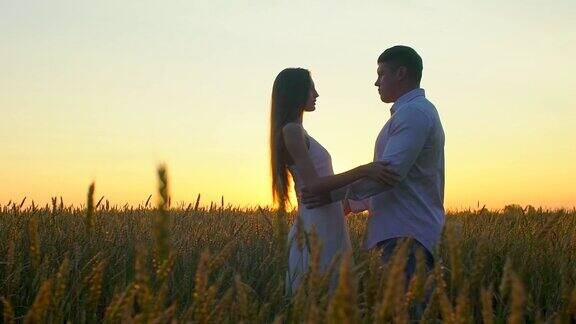 浪漫的年轻幸福的夫妇剪影在金色的麦田日落女人和男人在阳光下拥抱亲吻太阳镜头的光晕爱幸福的家庭自然户外慢镜头120fps