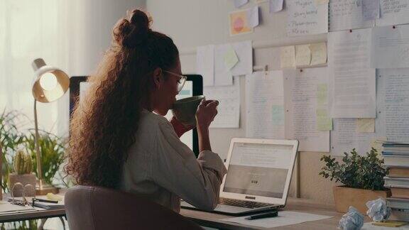 一段4k视频一名年轻女子一边喝咖啡一边在家里用笔记本电脑工作