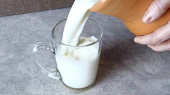 将牛奶从陶罐中倒入玻璃杯(特写)
