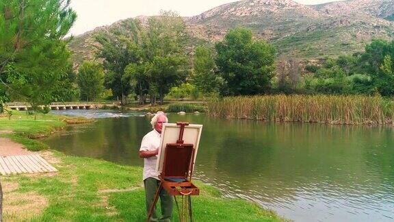 一位上了年纪的艺术家在秋天的河边的画架上画一幅画