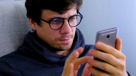 一名戴眼镜的男子正在用智能手机在社交媒体上输入信息脸部和手机特写
