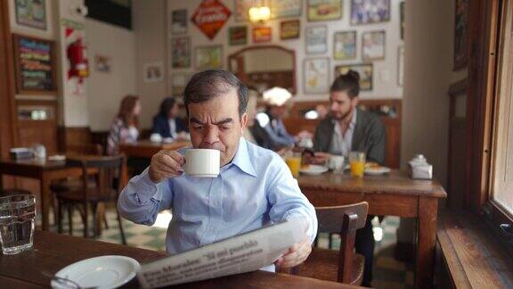 小个子男人一边喝咖啡一边看报纸看起来很困惑