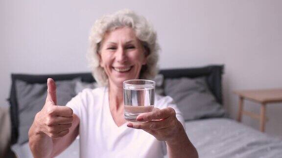 微笑的老妇人展示了一杯水竖起大拇指