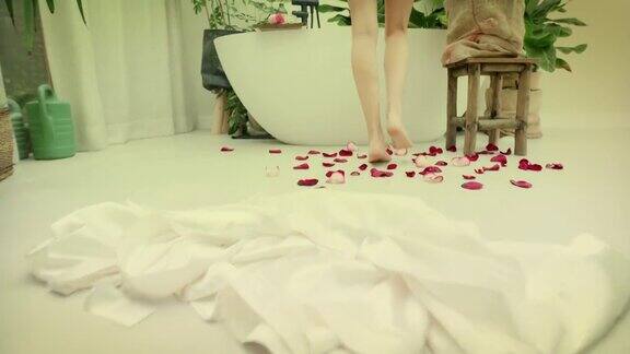 一个年轻的女人走进了她浴室里郁郁葱葱的绿色花园的泡泡浴特写她的双腿在玫瑰花瓣上行走