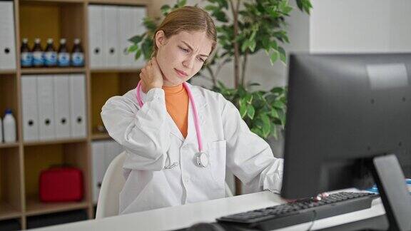 年轻的金发女医生在诊所用电脑忍受颈椎疼痛